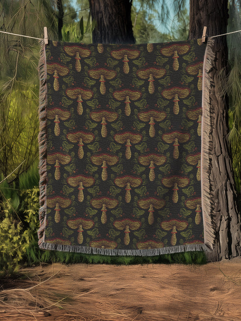 A woven cotton throw featuring an intricate mushroom and foliage pattern in deep charcoal and golden hues, framed by soft fringe.